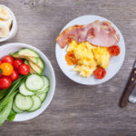 Breakfast: scrambled egg and bacon with salads, vegetables on a dark wooden table, selective focus